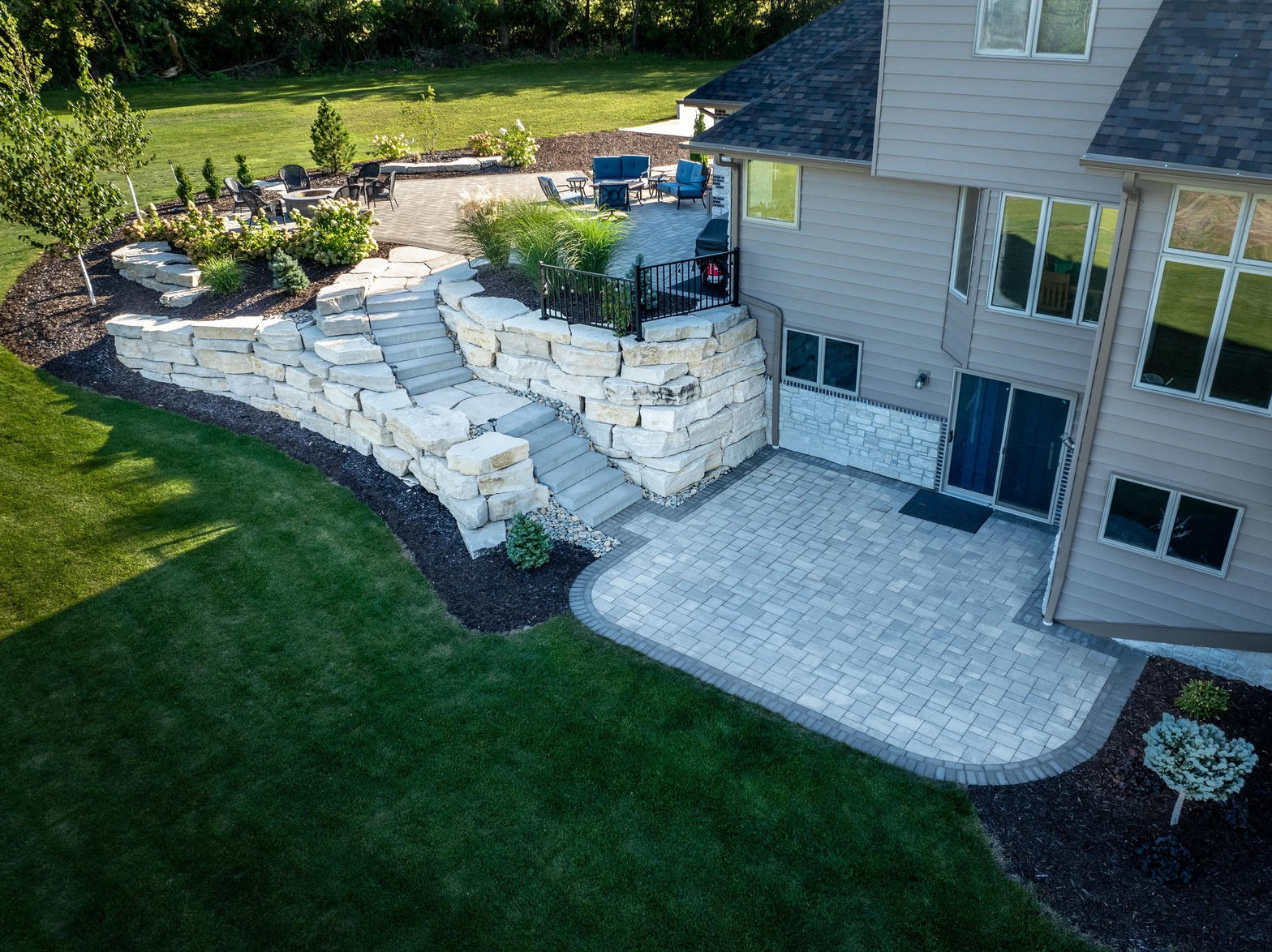 Stone retaining wall, paver patio, and planted beds