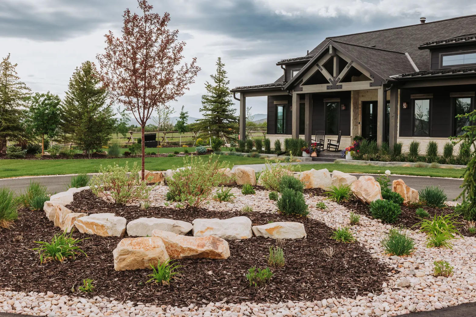 Front landscape with boulders, mulch, gravel, and new plantings